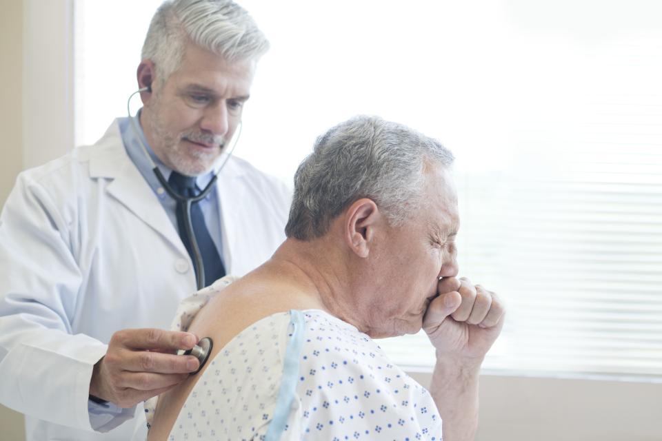 Male doctor examining coughing patient in hospital gown