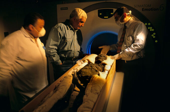 three researchers stand beside Tutankhamun’s mummy in front of a CT machine