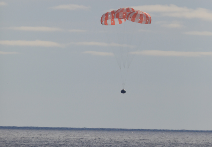 The spaceship Orion descended to the Pacific Ocean, slowed by a large red and white parachute