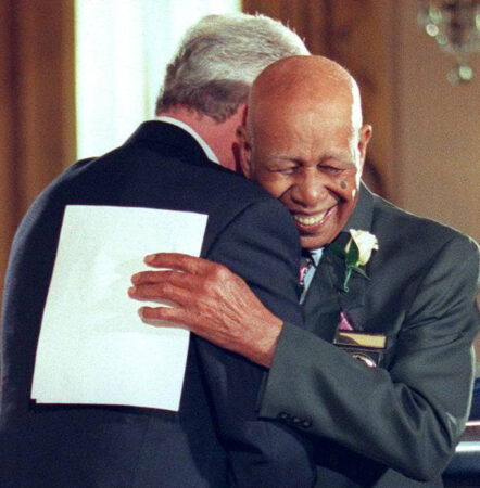 Herman Shaw holds a piece of paper as he hugs then-President Bill Clinton