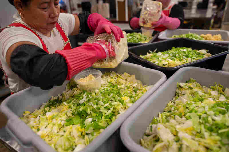 Employees at Tae Gu Kimchi top the brined cabbage with scallions and garlic on the second day of the kimchi-making process.
