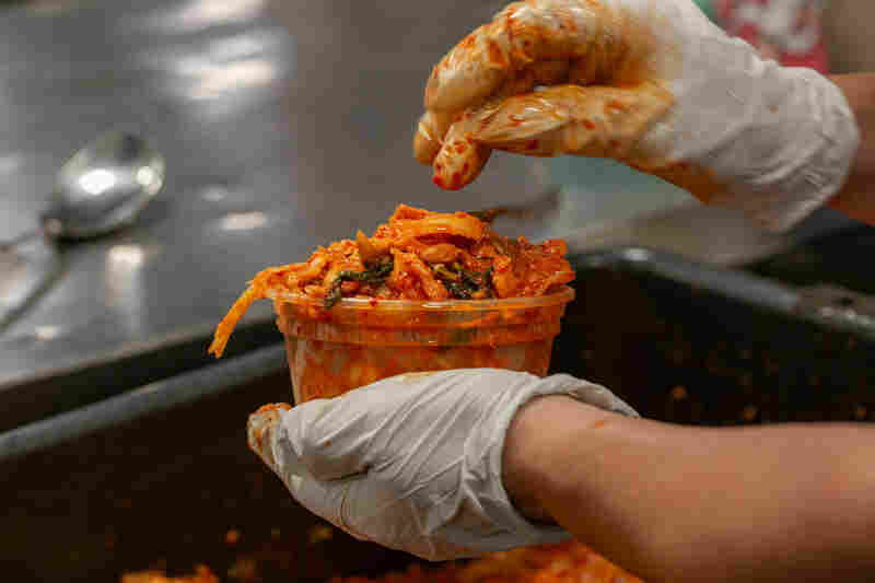 The mixed kimchi is scooped up and funneled into Tae Gu Kimchi packaging. The fermentation process continues once it's sealed up.